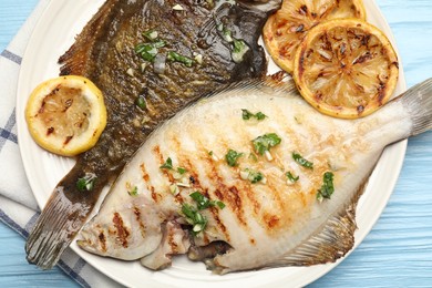 Photo of Tasty roasted flounder fish with herbs and lemon slices on light blue wooden table, closeup. Homemade seafood dish