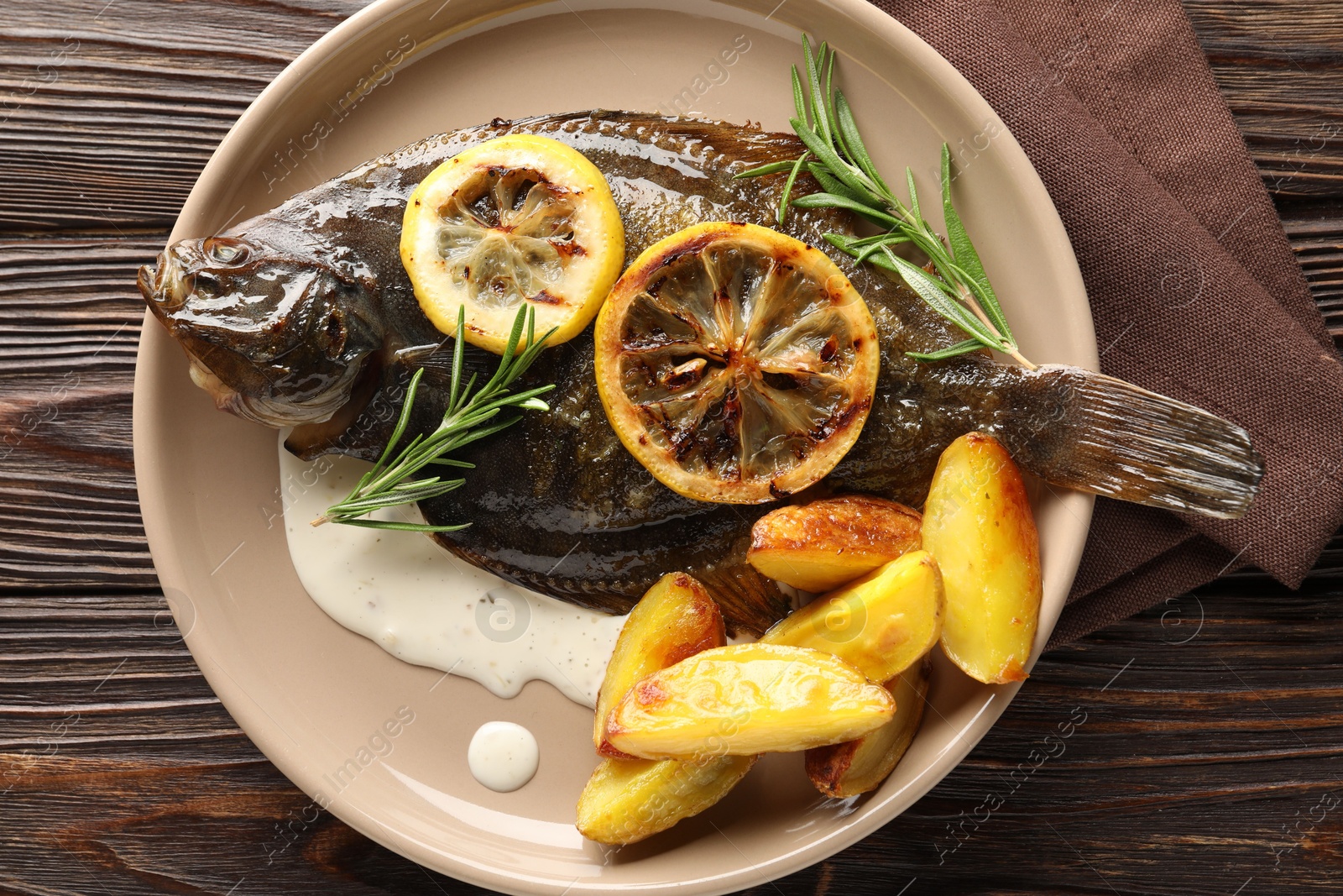 Photo of Tasty roasted flounder fish with rosemary, potato and lemon slices on wooden table, top view. Homemade seafood dish