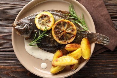 Photo of Tasty roasted flounder fish with rosemary, potato and lemon slices on wooden table, top view. Homemade seafood dish