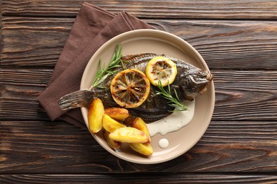 Photo of Tasty roasted flounder fish with rosemary, potato and lemon slices on wooden table, top view. Homemade seafood dish