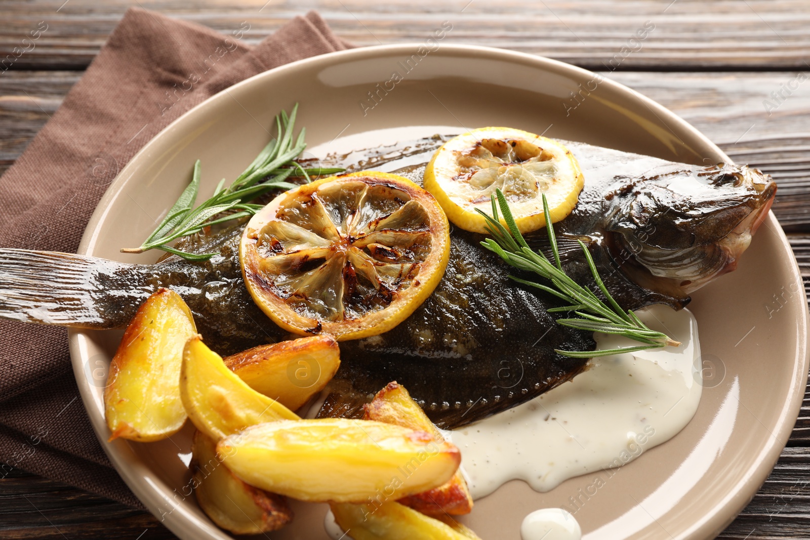 Photo of Tasty roasted flounder fish with rosemary, potato and lemon slices on wooden table, closeup. Homemade seafood dish