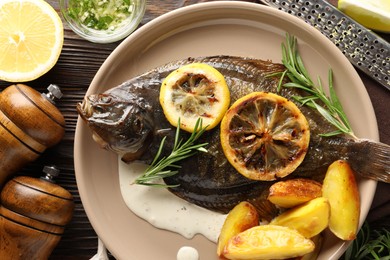 Photo of Tasty roasted flounder fish with rosemary, potato and lemon slices on wooden table, flat lay. Homemade seafood dish