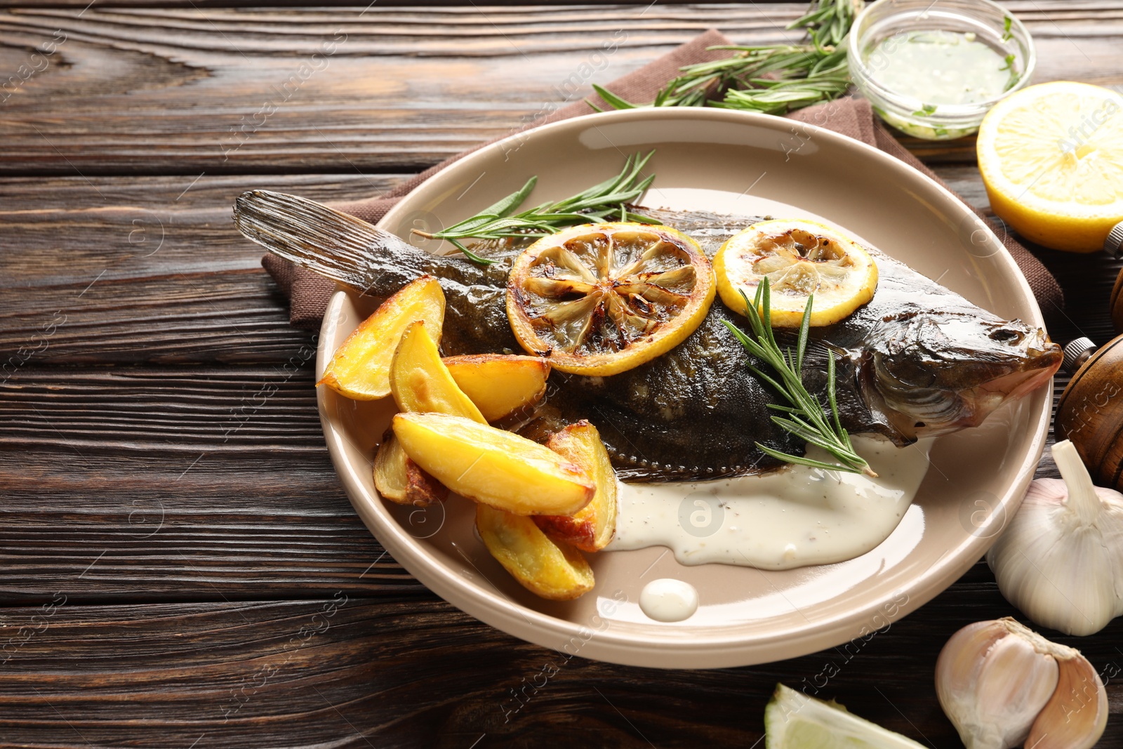 Photo of Tasty roasted flounder fish with rosemary, potato and lemon slices on wooden table, closeup. Homemade seafood dish