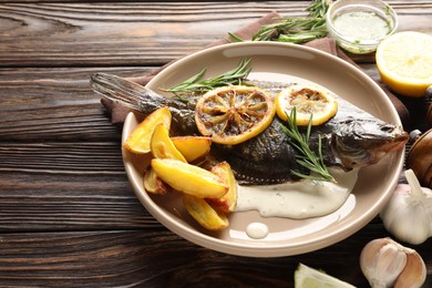 Photo of Tasty roasted flounder fish with rosemary, potato and lemon slices on wooden table, closeup. Homemade seafood dish