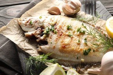 Photo of Tasty roasted flounder fish with spices served on wooden table, closeup. Homemade seafood dish