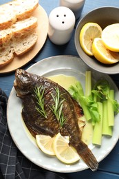 Photo of Tasty roasted flounder fish with celery served on blue table, flat lay. Homemade seafood dish