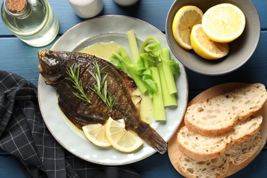 Photo of Tasty roasted flounder fish with celery served on blue wooden table, flat lay. Homemade seafood dish
