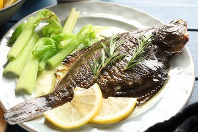 Photo of Tasty roasted flounder fish with celery served on blue wooden table, closeup. Homemade seafood dish