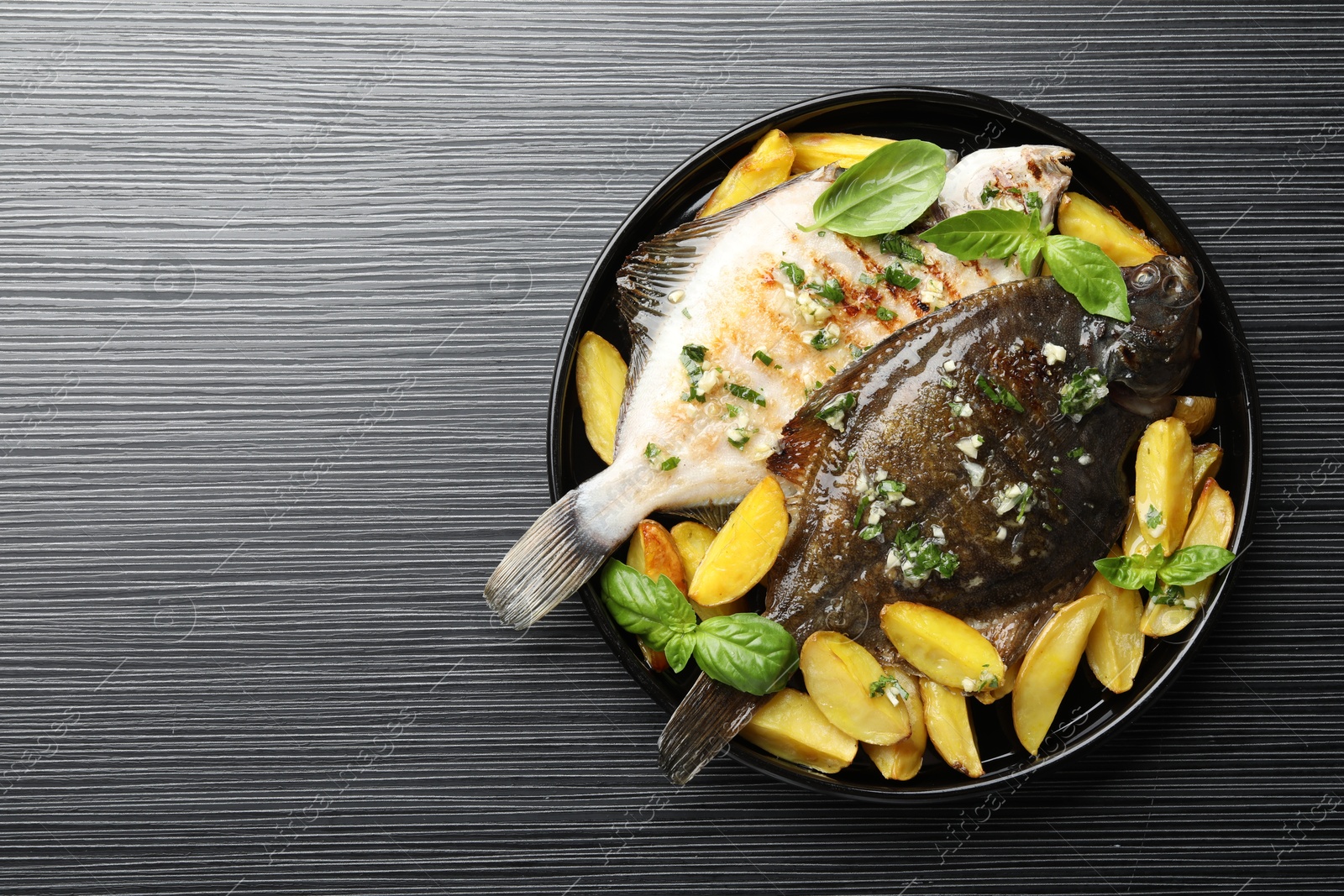 Photo of Homemade seafood dish. Tasty roasted flounder fish with herbs and potato on black table, top view. Space for text