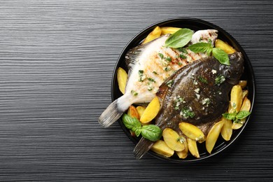 Photo of Homemade seafood dish. Tasty roasted flounder fish with herbs and potato on black table, top view. Space for text