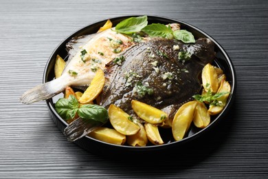 Photo of Tasty roasted flounder fish with herbs and potato on black table, closeup. Homemade seafood dish
