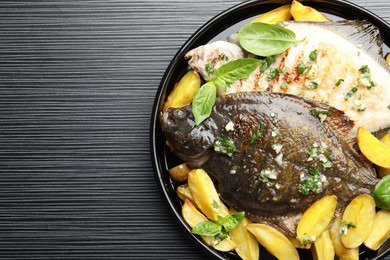 Photo of Homemade seafood dish. Tasty roasted flounder fish with herbs and potato on black table, top view. Space for text