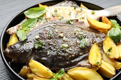 Photo of Tasty roasted flounder fish with herbs and potato on black table, closeup. Homemade seafood dish
