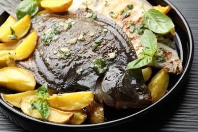 Photo of Tasty roasted flounder fish with herbs and potato on black table, closeup. Homemade seafood dish