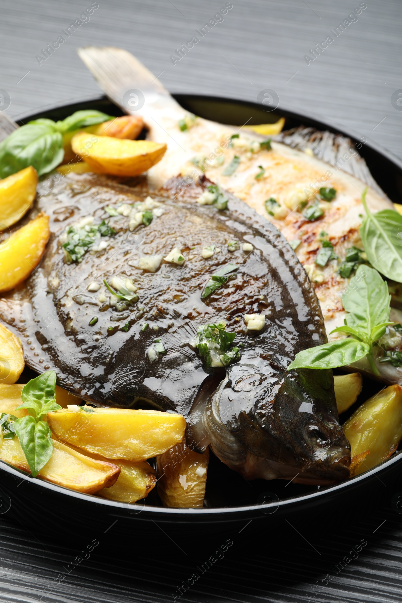 Photo of Tasty roasted flounder fish with herbs and potato on black table, closeup. Homemade seafood dish