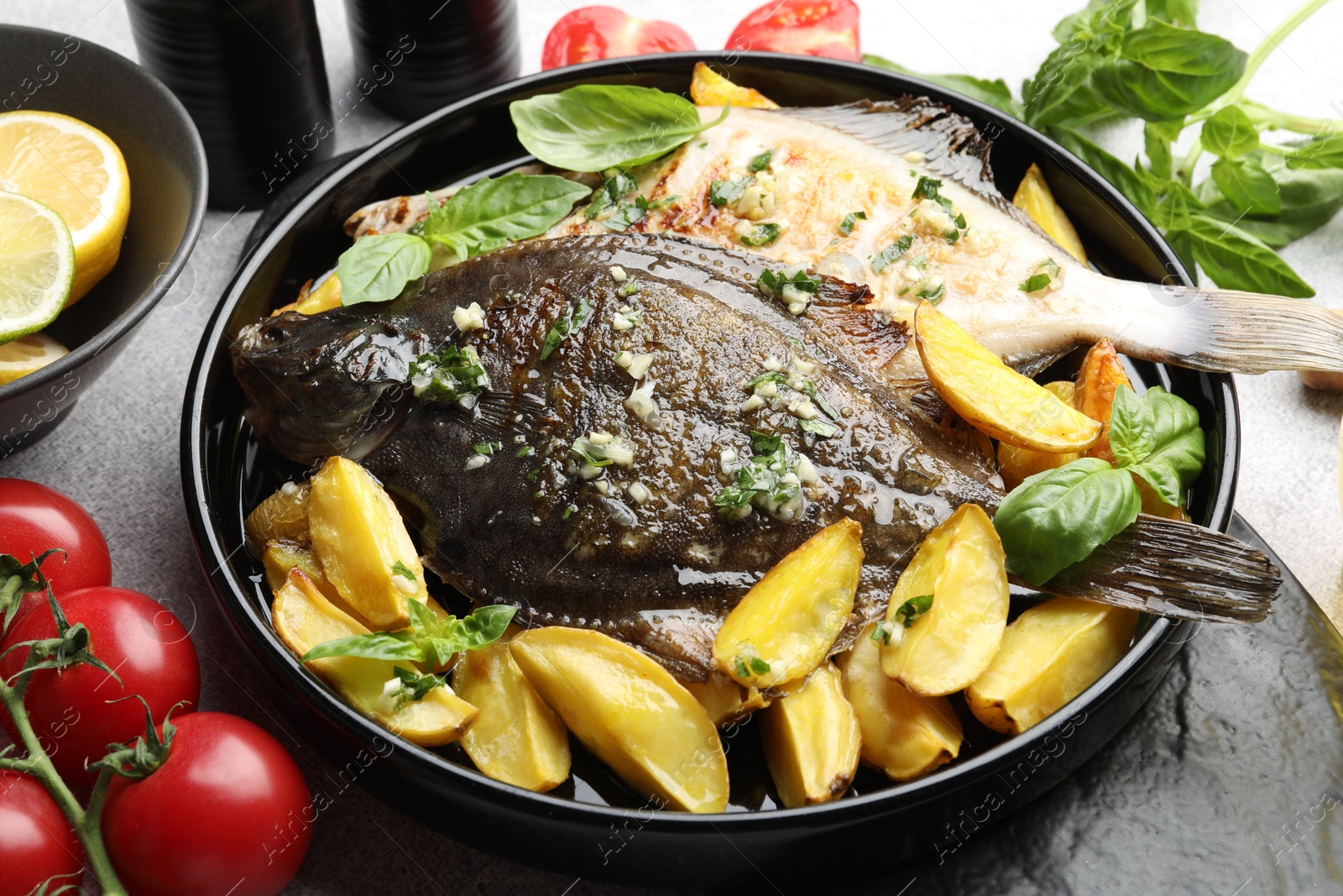 Photo of Tasty roasted flounder fish with herbs, potato, lemon slices and tomatoes on light table, closeup. Homemade seafood dish