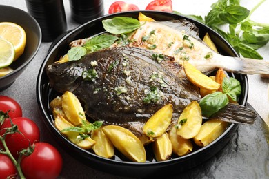 Photo of Tasty roasted flounder fish with herbs, potato, lemon slices and tomatoes on light table, closeup. Homemade seafood dish