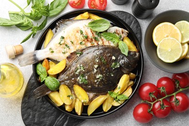 Photo of Tasty roasted flounder fish with herbs, potato, lemon slices and tomatoes on light table, flat lay. Homemade seafood dish