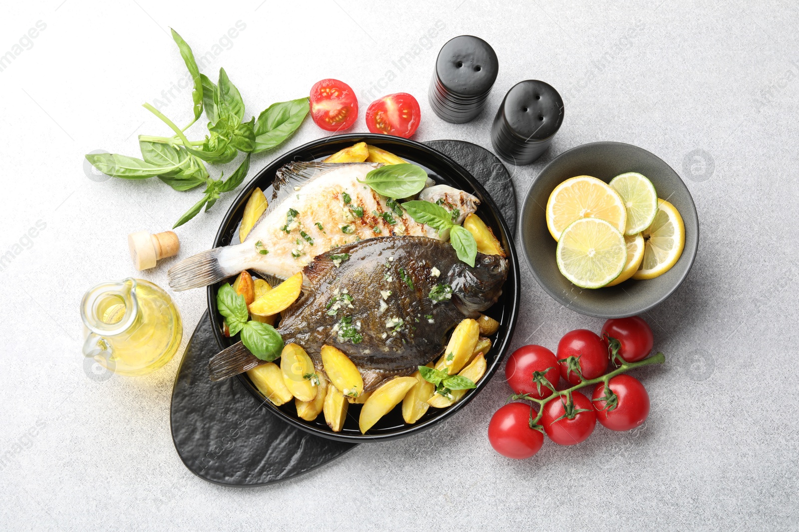 Photo of Tasty roasted flounder fish with herbs, potato, lemon slices and tomatoes on light table, flat lay. Homemade seafood dish