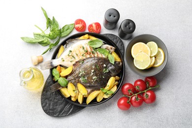 Photo of Tasty roasted flounder fish with herbs, potato, lemon slices and tomatoes on light table, flat lay. Homemade seafood dish