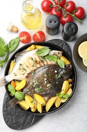 Photo of Tasty roasted flounder fish with herbs, potato, lemon slices and tomatoes on light table, flat lay. Homemade seafood dish