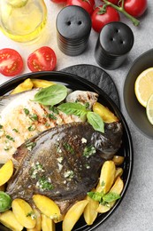 Photo of Tasty roasted flounder fish with herbs, potato, lemon slices and tomatoes on light table, flat lay. Homemade seafood dish