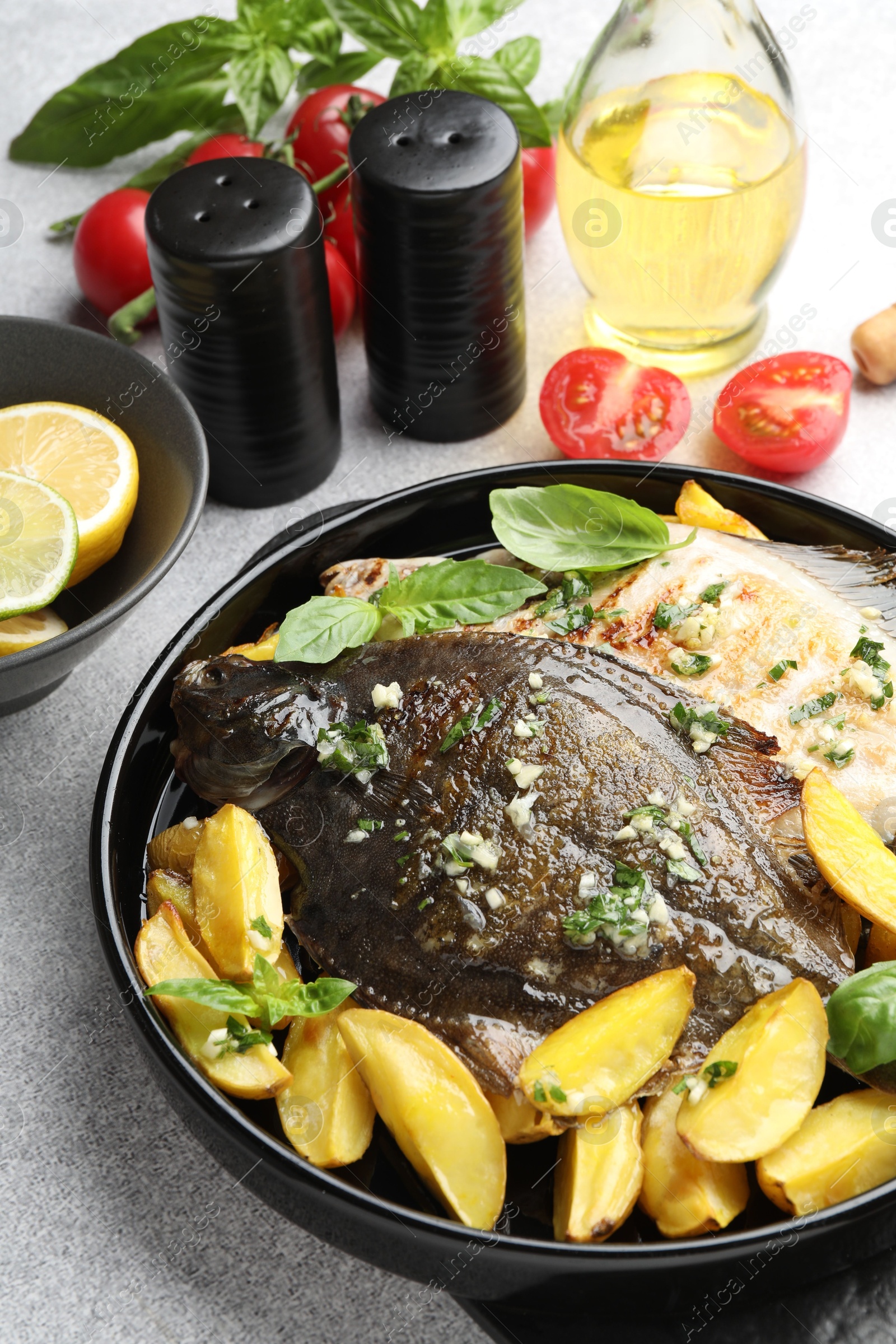 Photo of Tasty roasted flounder fish with herbs, potato and tomatoes on light table, closeup. Homemade seafood dish
