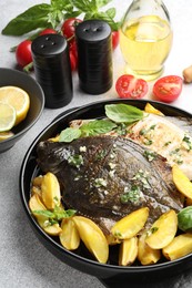 Photo of Tasty roasted flounder fish with herbs, potato and tomatoes on light table, closeup. Homemade seafood dish