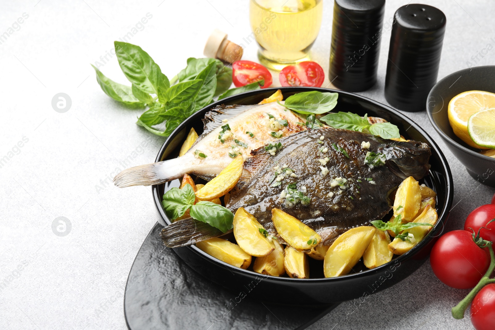 Photo of Tasty roasted flounder fish with herbs, potato and tomatoes on light table, closeup. Homemade seafood dish