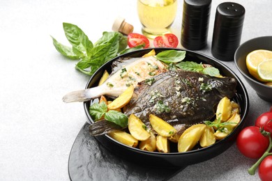Photo of Tasty roasted flounder fish with herbs, potato and tomatoes on light table, closeup. Homemade seafood dish