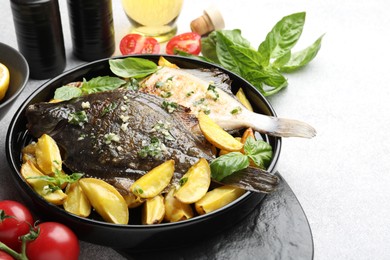 Photo of Tasty roasted flounder fish with herbs, potato and tomatoes on light table, closeup. Homemade seafood dish
