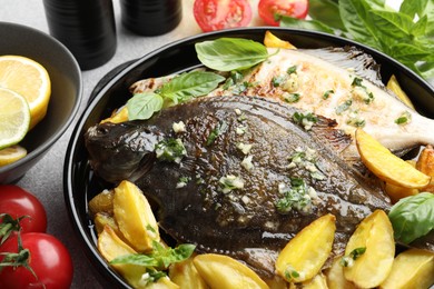 Photo of Tasty roasted flounder fish with herbs, potato, lemon slices and tomatoes on light table, closeup. Homemade seafood dish