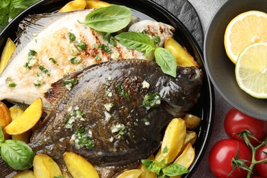 Photo of Tasty roasted flounder fish with herbs, potato, lemon slices and tomatoes on light table, flat lay. Homemade seafood dish