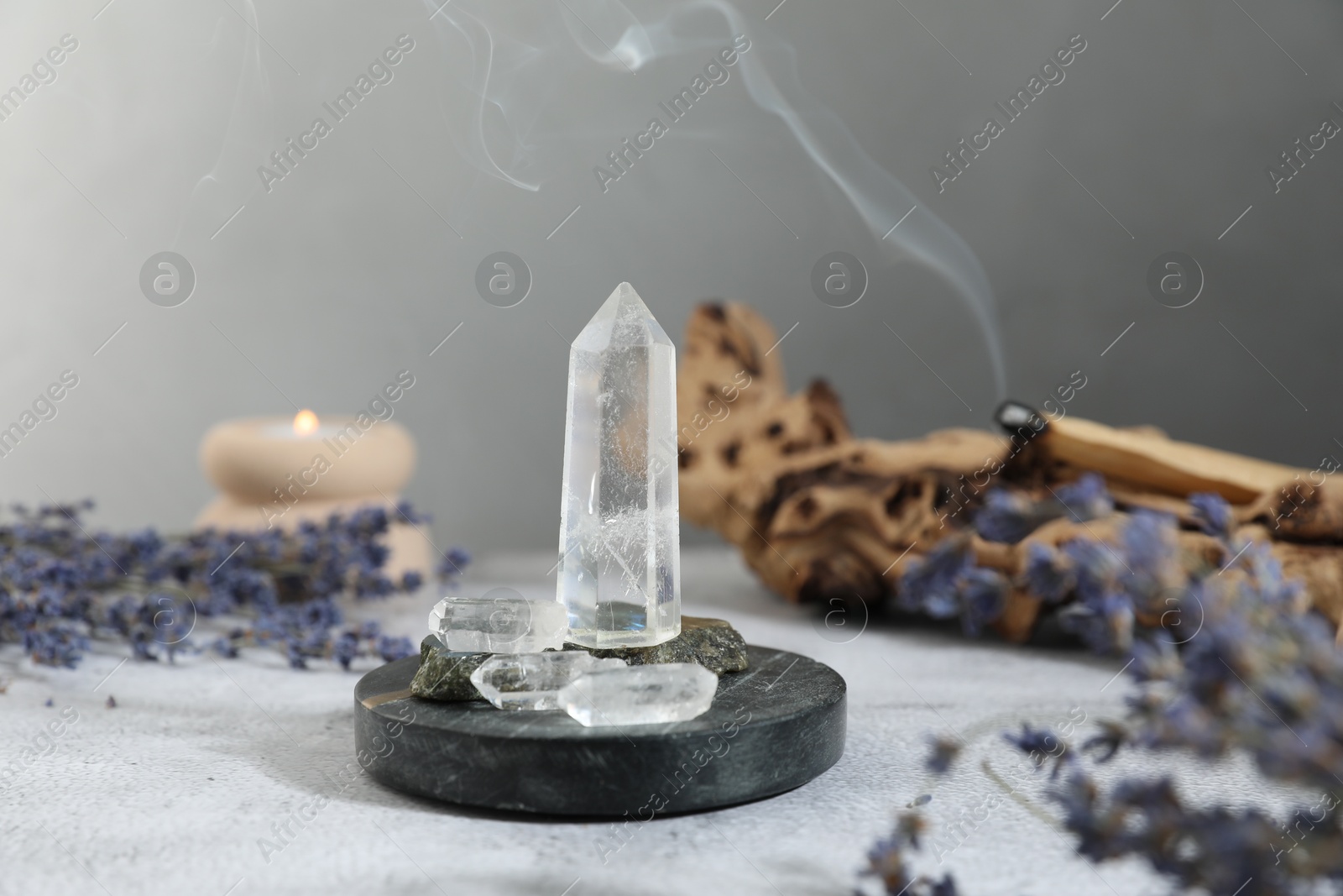 Photo of Aura. Different crystals, lavender, burning candle and Palo Santo on white textured table