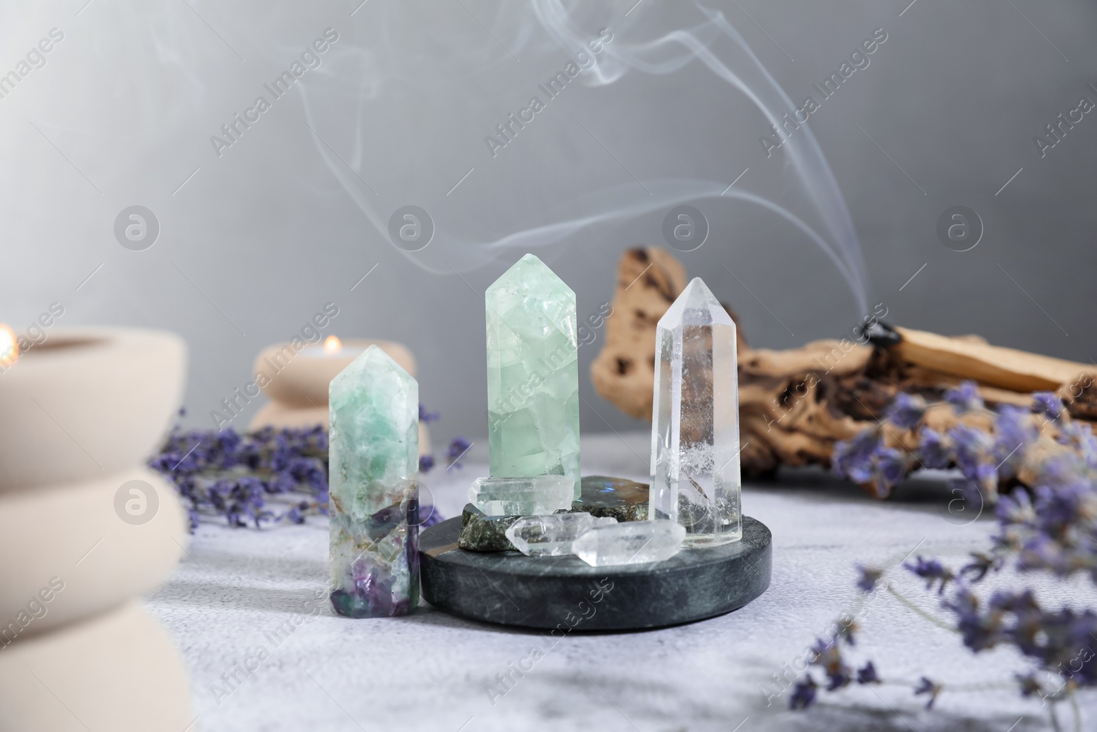 Photo of Aura. Different crystals, lavender, burning candles and Palo Santo stick on white textured table