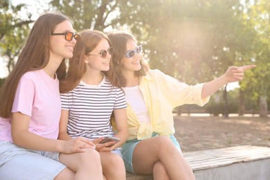 Photo of Happy friends in sunglasses on bench outdoors