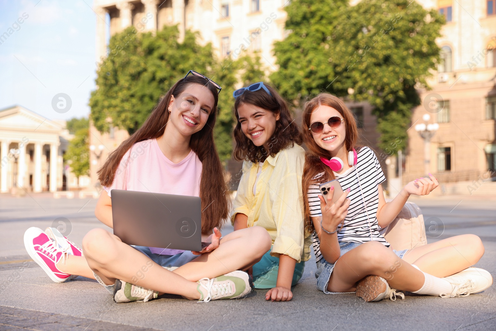Happy friends with laptop on asphalt outdoors Photo of Happy friends with laptop on asphalt outdoors