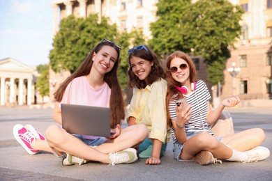 Photo of Happy friends with laptop on asphalt outdoors