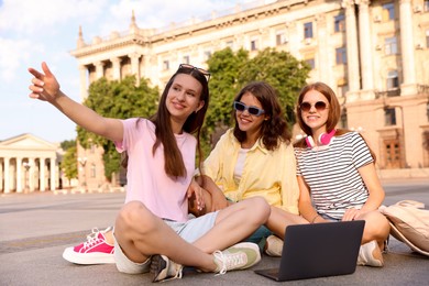 Photo of Happy friends with laptop on asphalt outdoors