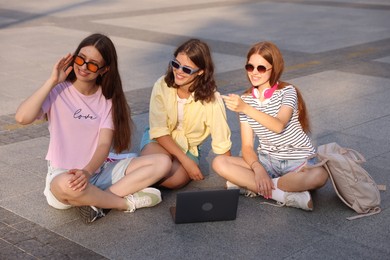Photo of Happy friends with laptop on asphalt outdoors