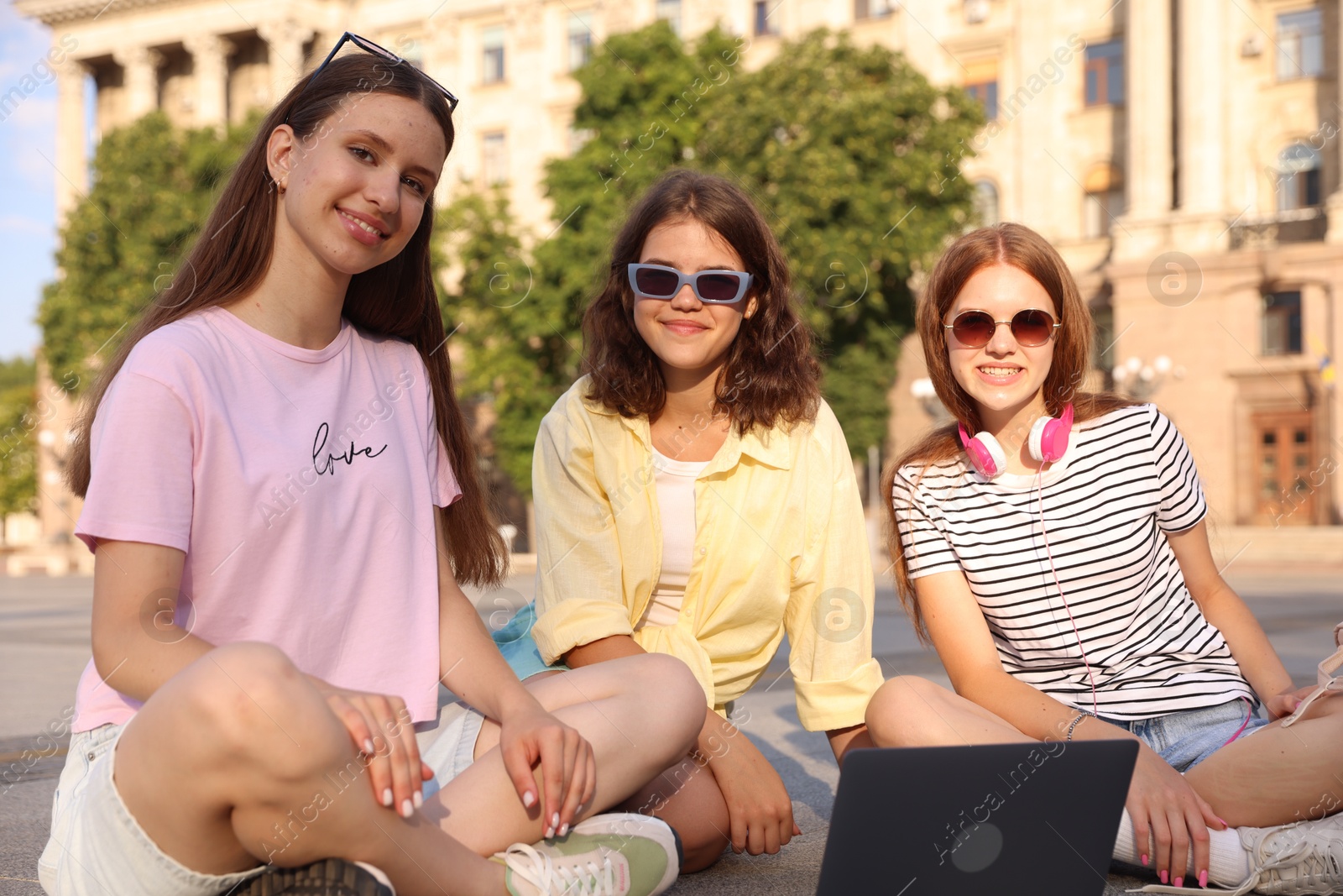 Happy friends with laptop on asphalt outdoors Photo of Happy friends with laptop on asphalt outdoors