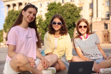 Photo of Happy friends with laptop on asphalt outdoors