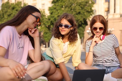 Photo of Three friends watching something on laptop outdoors