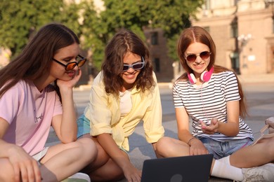 Photo of Three friends watching something on laptop outdoors