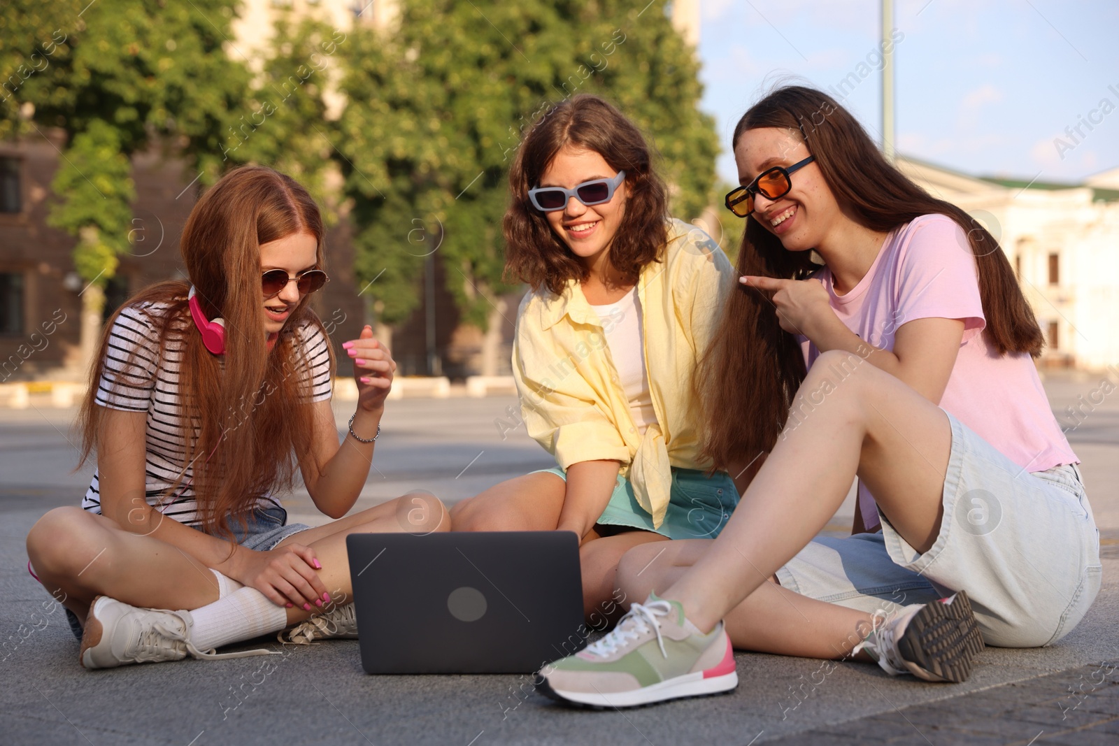 Three friends watching something on laptop outdoors Photo of Three friends watching something on laptop outdoors