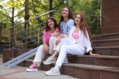 Photo of Three happy friends sitting on stairs outdoors