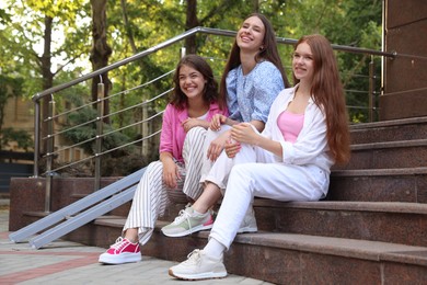 Photo of Three happy friends sitting on stairs outdoors