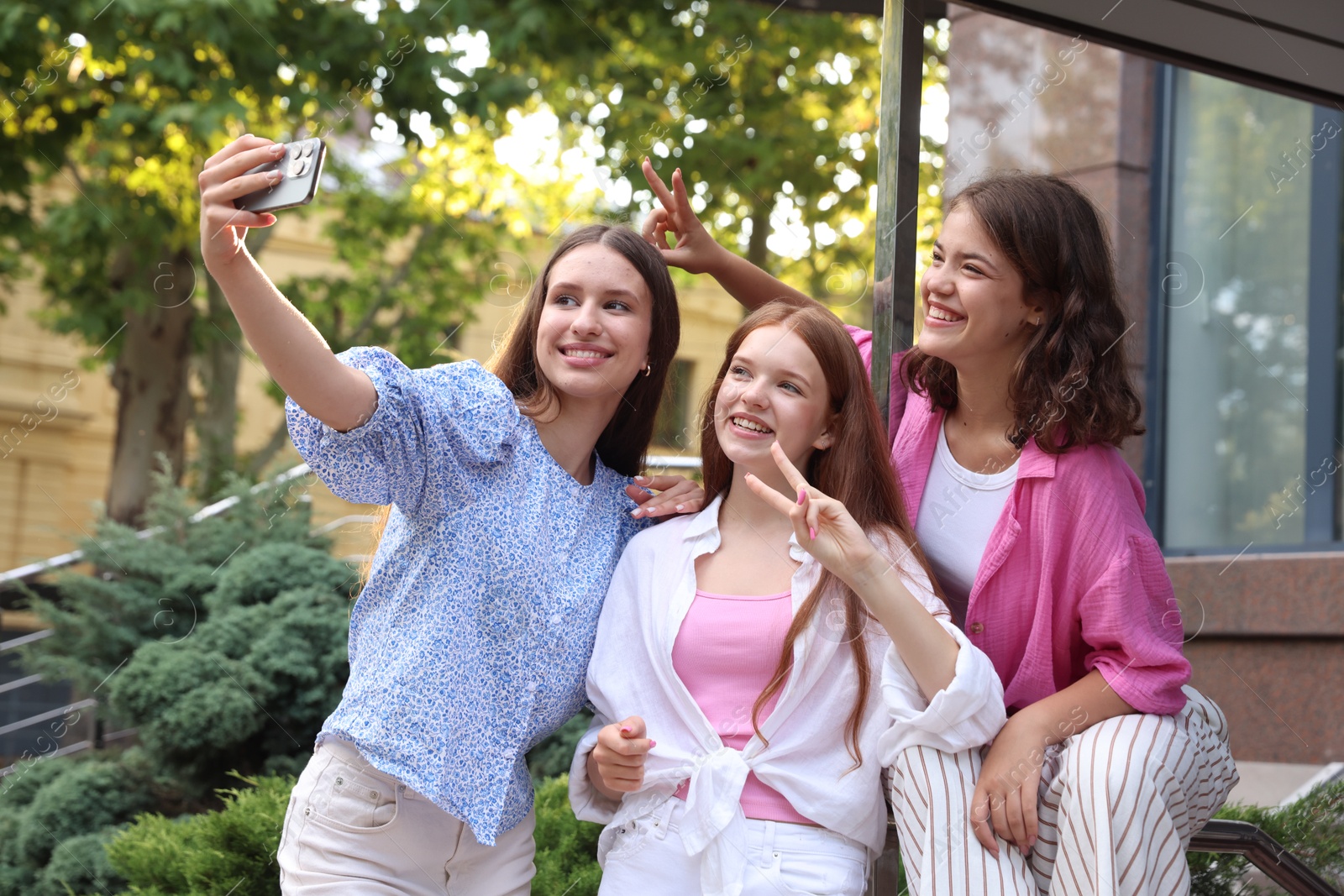 Photo of Happy friends taking selfie with smartphone near building outdoors