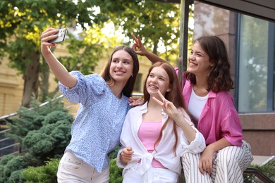 Photo of Happy friends taking selfie with smartphone near building outdoors