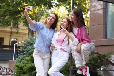 Photo of Happy friends taking selfie with smartphone near building outdoors